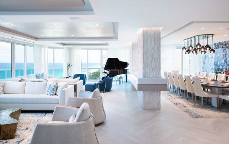 Sarah-Z-Designs - A view to the ocean around the house, a black piano, a white sofa, two armchairs and a dining table with dining chairs.